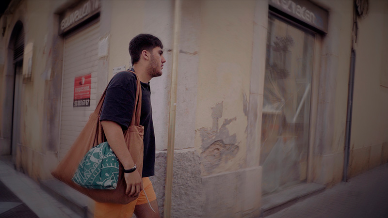 Fotograma de DUES CARES: el protagonista camina pel carrer amb una bossa a l'espatlla