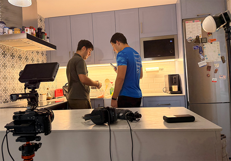Making-of de DUES CARES: dos membres de l'equip preparen una escena a la cuina amb la càmera en primer pla